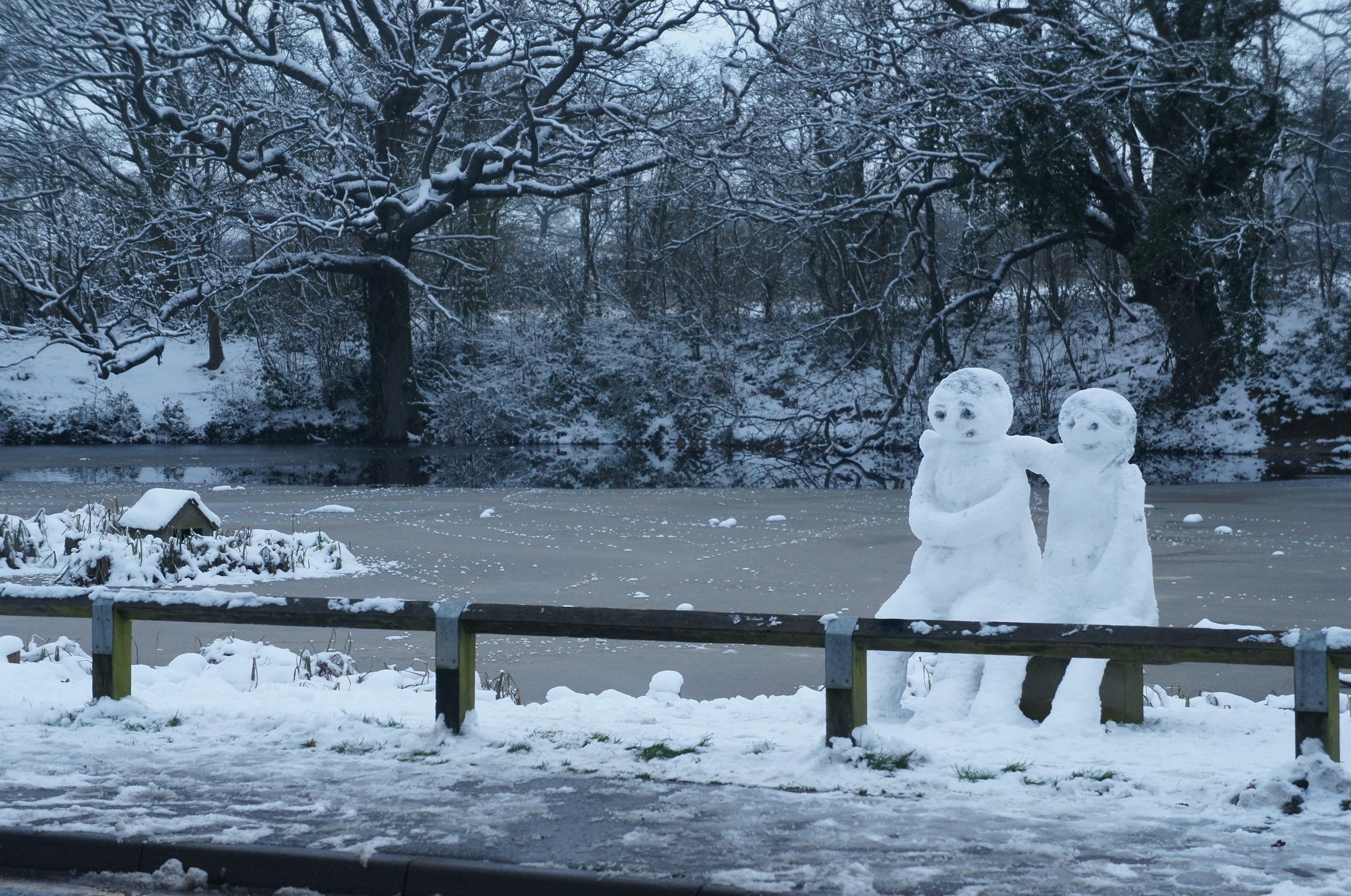 The village pond frozen over in winter, with two snow figures on the bank